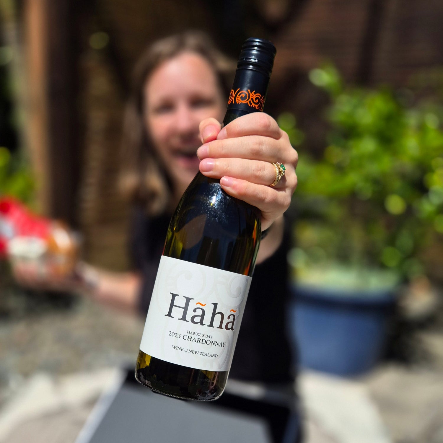 Woman holding up a bottle of Hāhā Chardonnay from a Wickedly Indulgent gift box, celebrating Kiwi wine and sunshine — the perfect gift from overseas to New Zealand.