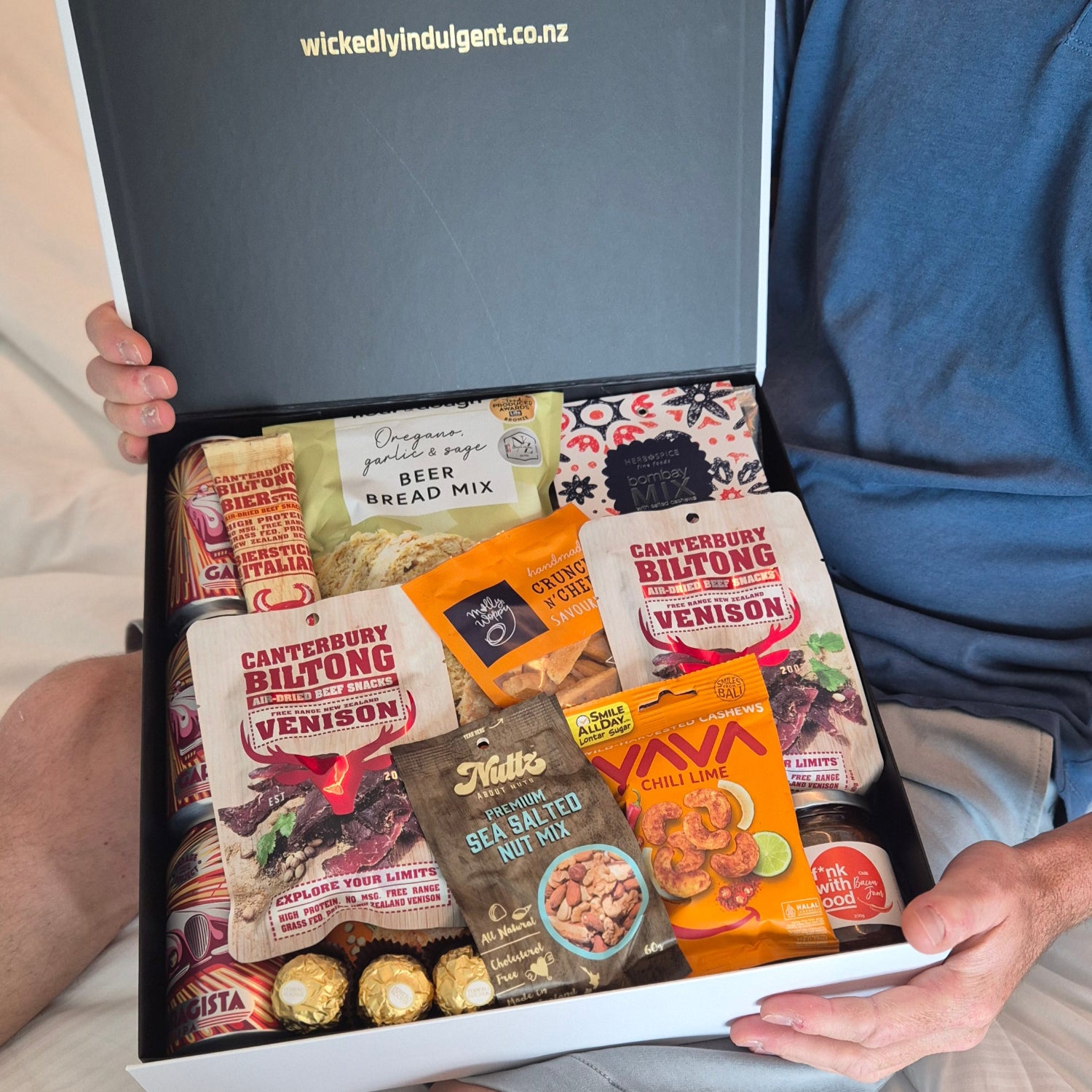 Man opening a Wickedly Indulgent savoury gift hamper filled with venison biltong, beer bread mix, and artisan snacks — perfect for bold gifting in Invercargill and beyond.