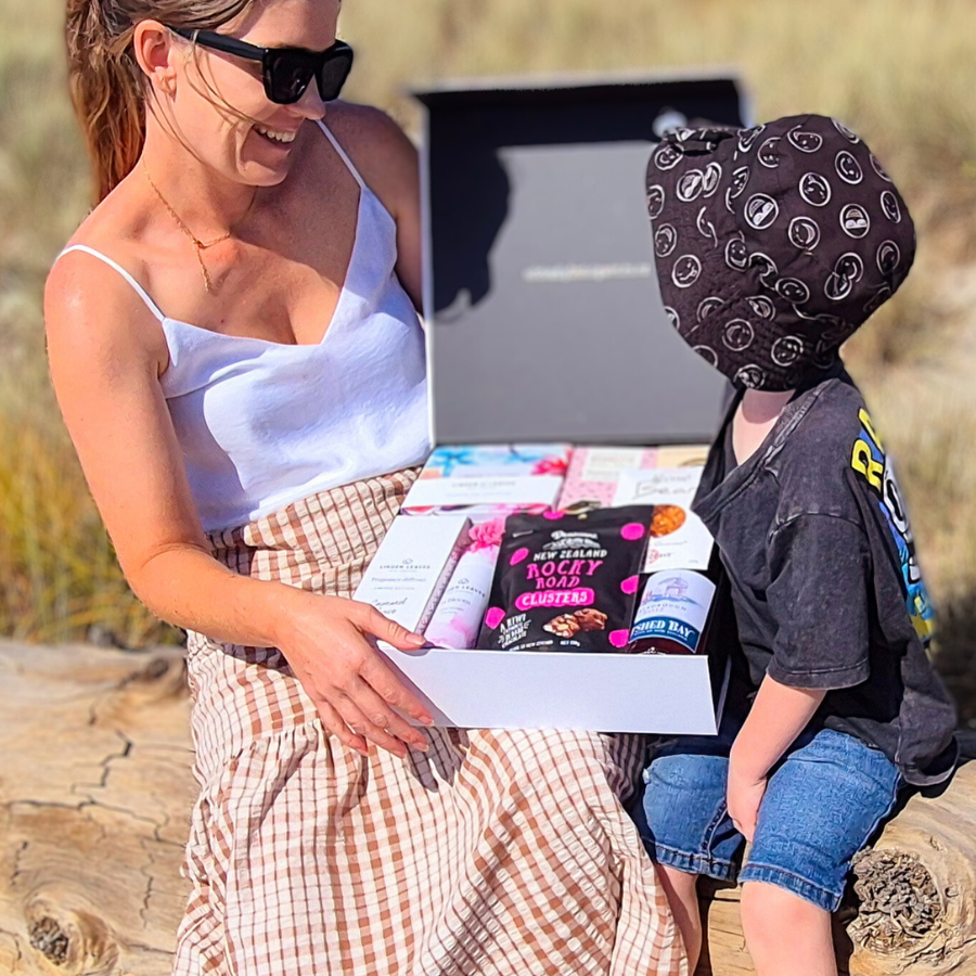 Woman and child opening a birthday gift hamper outdoors, filled with NZ snacks and pamper treats . Wickedly Indulgent moment.