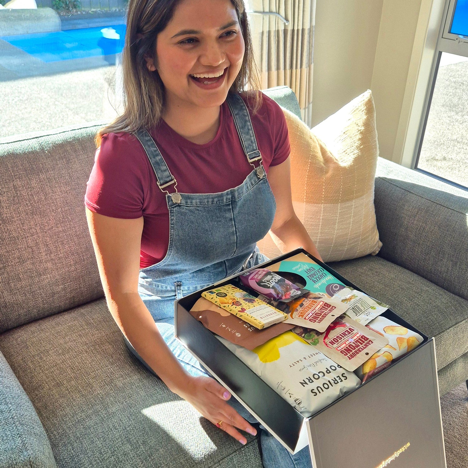 Happy recipient opening a gluten free and dairy free gift hamper with chocolate, popcorn, chips and allergy-friendly treats.