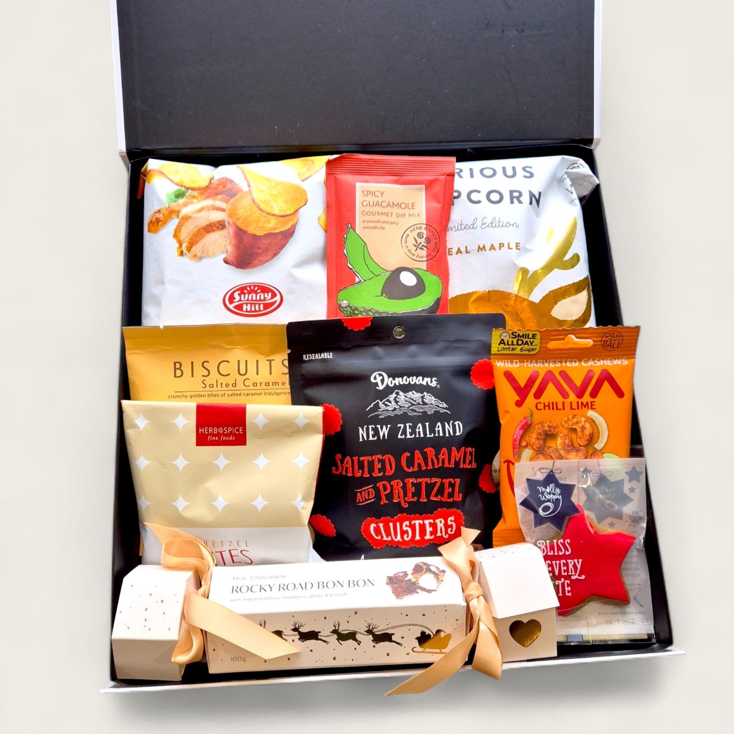 Christmas gift hamper with Biscoff rocky road, popcorn, kumara chips, chocolate clusters, and festive treats in a black box with ribbon.