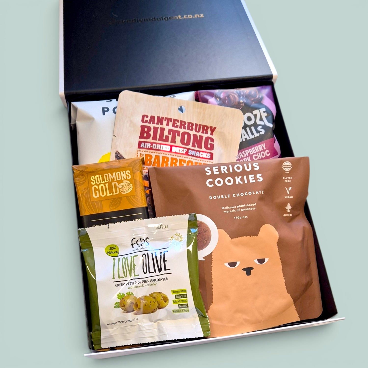 Snaccidents Happen gluten-free dairy-free gift box NZ, with Canterbury Biltong, Frooze Balls, Serious Cookies Double Chocolate, Solomons Gold chocolate, pitted olives and Serious Popcorn packed inside a black and white Wickedly Indulgent gift box