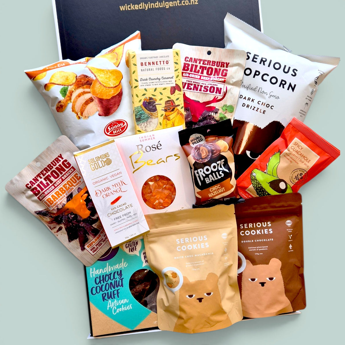 Wickedly Indulgent GF Treats on Repeat gluten-free snack gift box NZ 
with Canterbury Biltong, Bennetto chocolate, Solomon's Gold vegan 
chocolate, Serious Popcorn, Serious Cookies and Frooze Balls in a 
black & white gift box