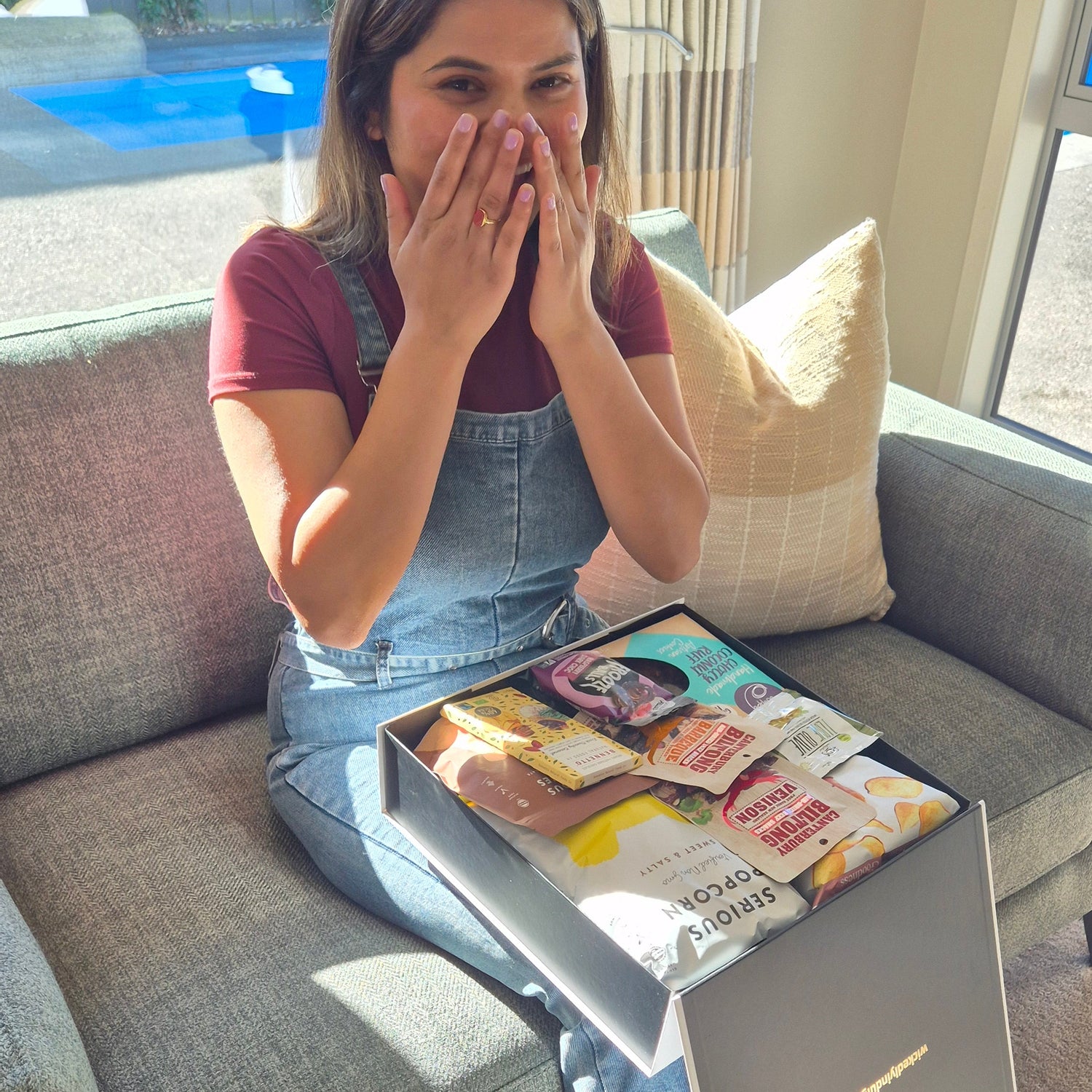 Happy recipient reacting to a gluten free gift hamper packed with sweet and savoury treats in a premium Wickedly Indulgent gift box.