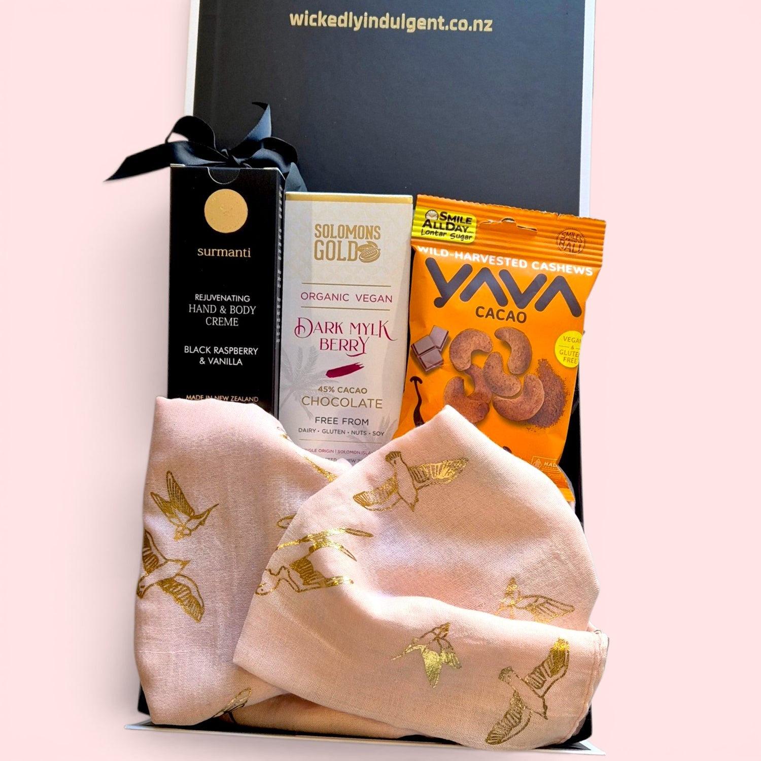 Dairy and gluten free gift box for her containing a pink scarf with gold 
bird print, Surmanti natural hand cream, Solomon's Gold vegan chocolate 
tablet, and Yava cacao-coated cashews, presented in a sleek black gift  box with satin ribbon, by Wickedly Indulgent, New Zealand