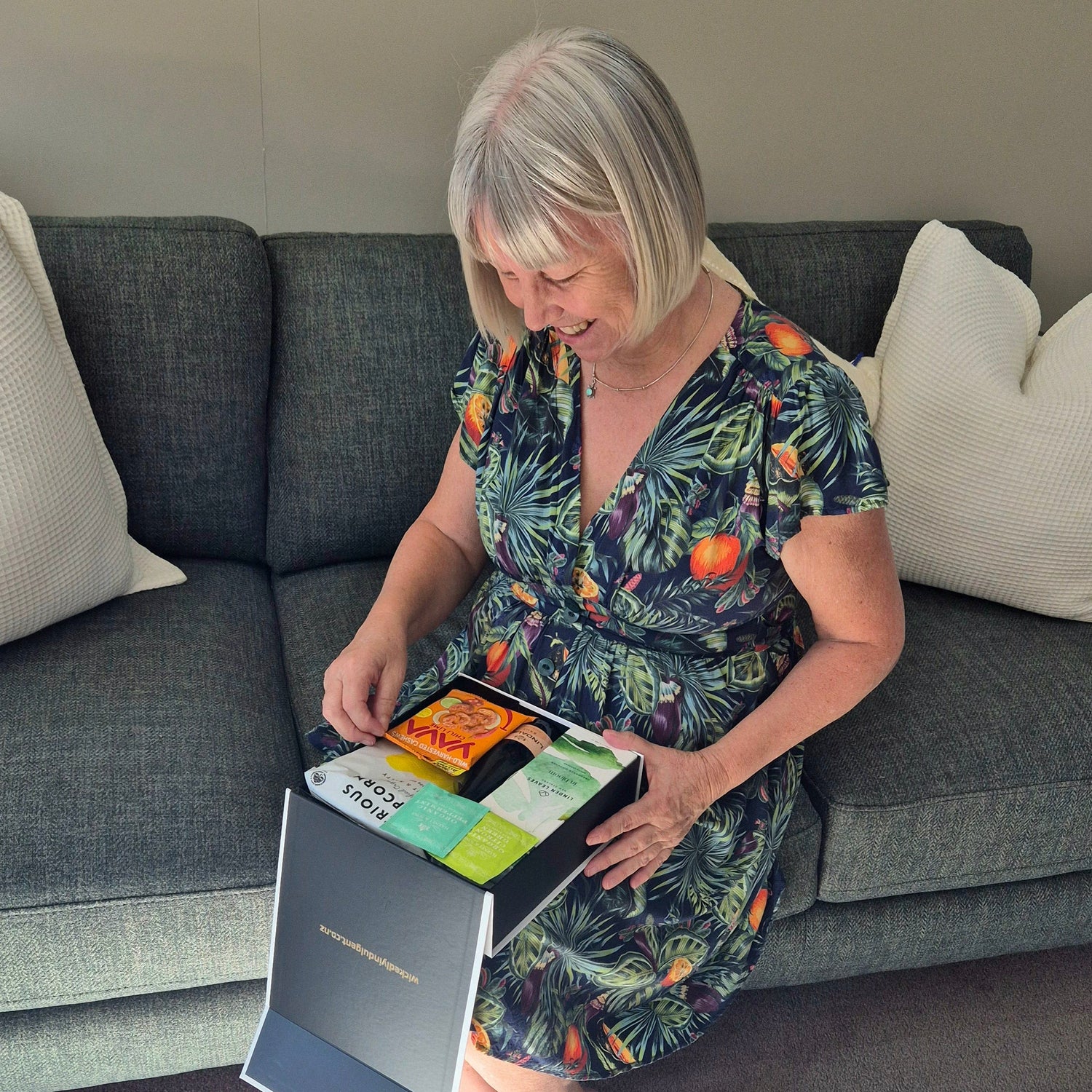 Smiling recipient enjoying a gluten free gift box filled with wine and gourmet treats, perfect for thoughtful NZ gift delivery.