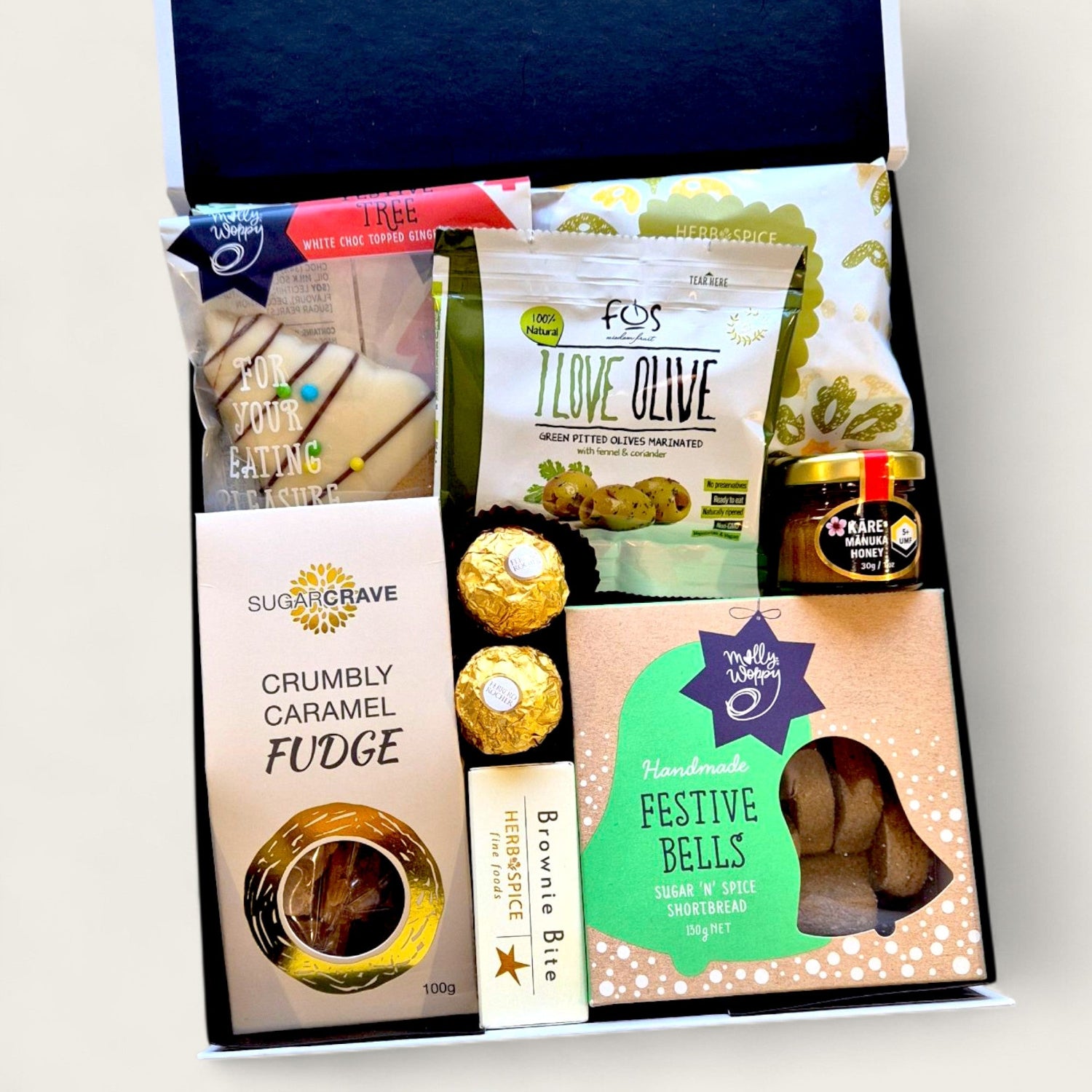 Festive Christmas hamper filled with premium snacks and treats including dark mint chocolate, caramel fudge, festive shortbread bells, Ferrero Rocher, savoury pretzels, olives, honey, brownie bite, and a decorated gingerbread tree cookie.