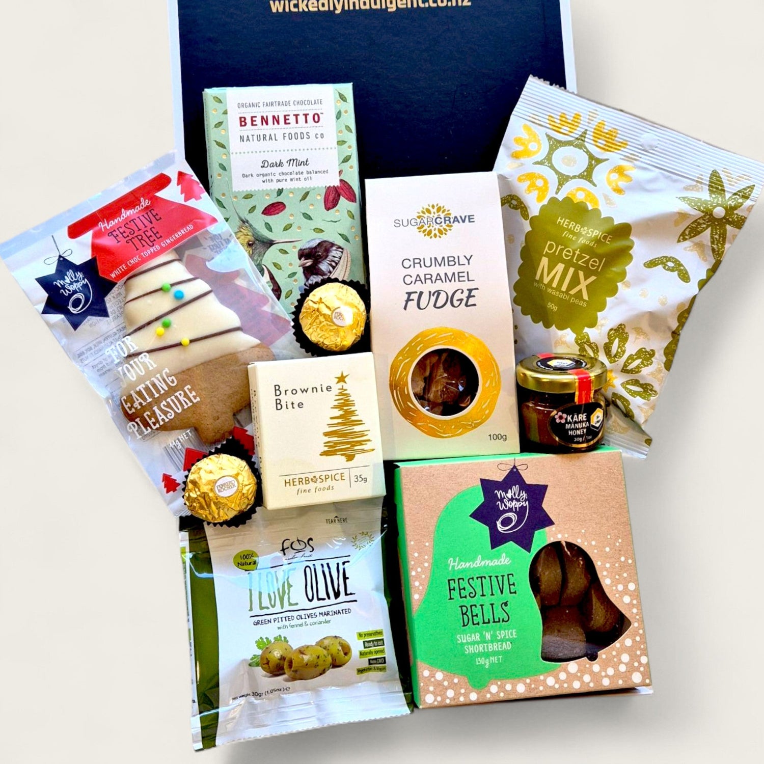 Festive Christmas hamper filled with premium snacks and treats including dark mint chocolate, caramel fudge, festive shortbread bells, Ferrero Rocher, savoury pretzels, olives, honey, brownie bite, and a decorated gingerbread tree cookie.