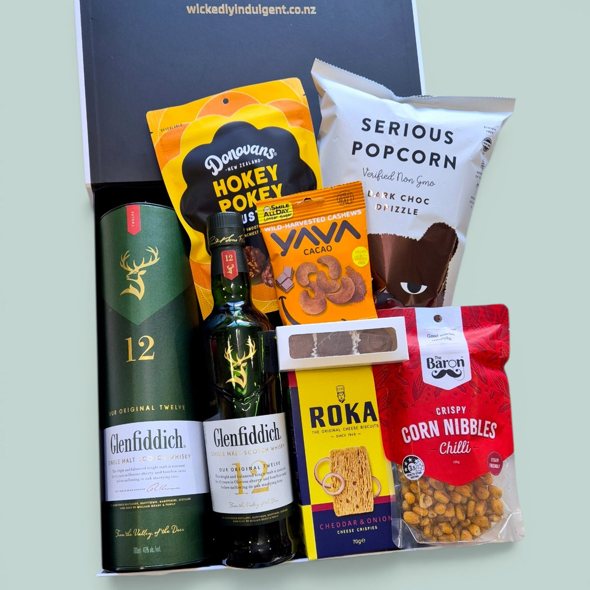 Men's whisky gift box containing Glenfiddich 12 Year Scotch whisky 
bottles, Serious Popcorn, Yava cacao cashews, Donovan's chocolates, Roka cheese biscuits, and The Barn corn nibbles, presented in a 
black gift box, Wickedly Indulgent NZ