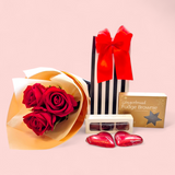 Black-and-white gift bag filled with a chocolate treat and a gingerbread brownie, accompanied by three beautifully wrapped artificial red roses, perfect for Valentine’s Day gifting.