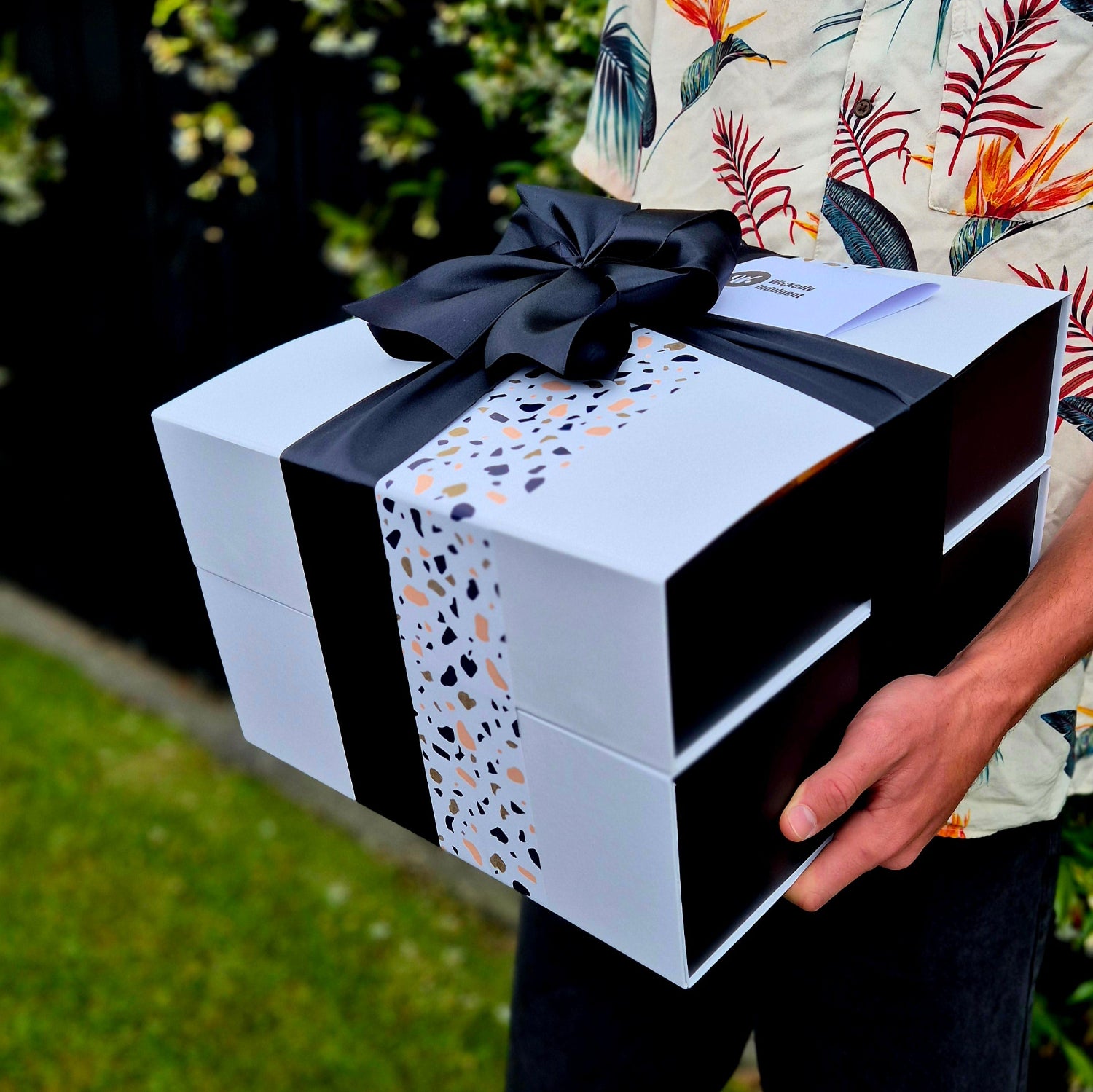 Birthday gift hamper with terrazzo wrap and black ribbon, held ready for delivery – premium NZ birthday box by Wickedly Indulgent.