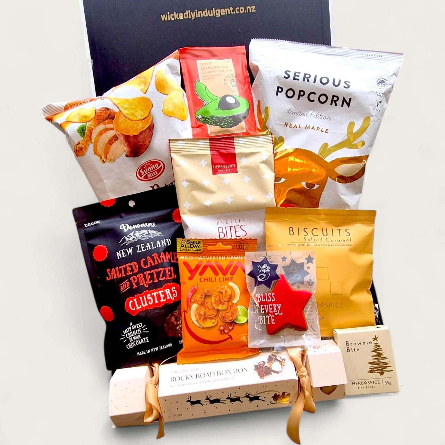 Christmas gift hamper with Biscoff rocky road, popcorn, kumara chips, chocolate clusters, and festive treats in a black box with ribbon.