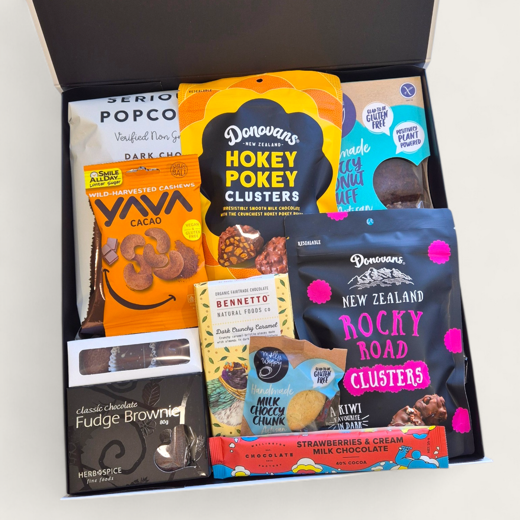A premium gift hamper called "For Choc’s Sake" featuring chocolate treats including popcorn, cookies, rocky road, artisan  chocolate, borwnie, and cacao cashews in a sleek black & white Wickedly Indulgent box.