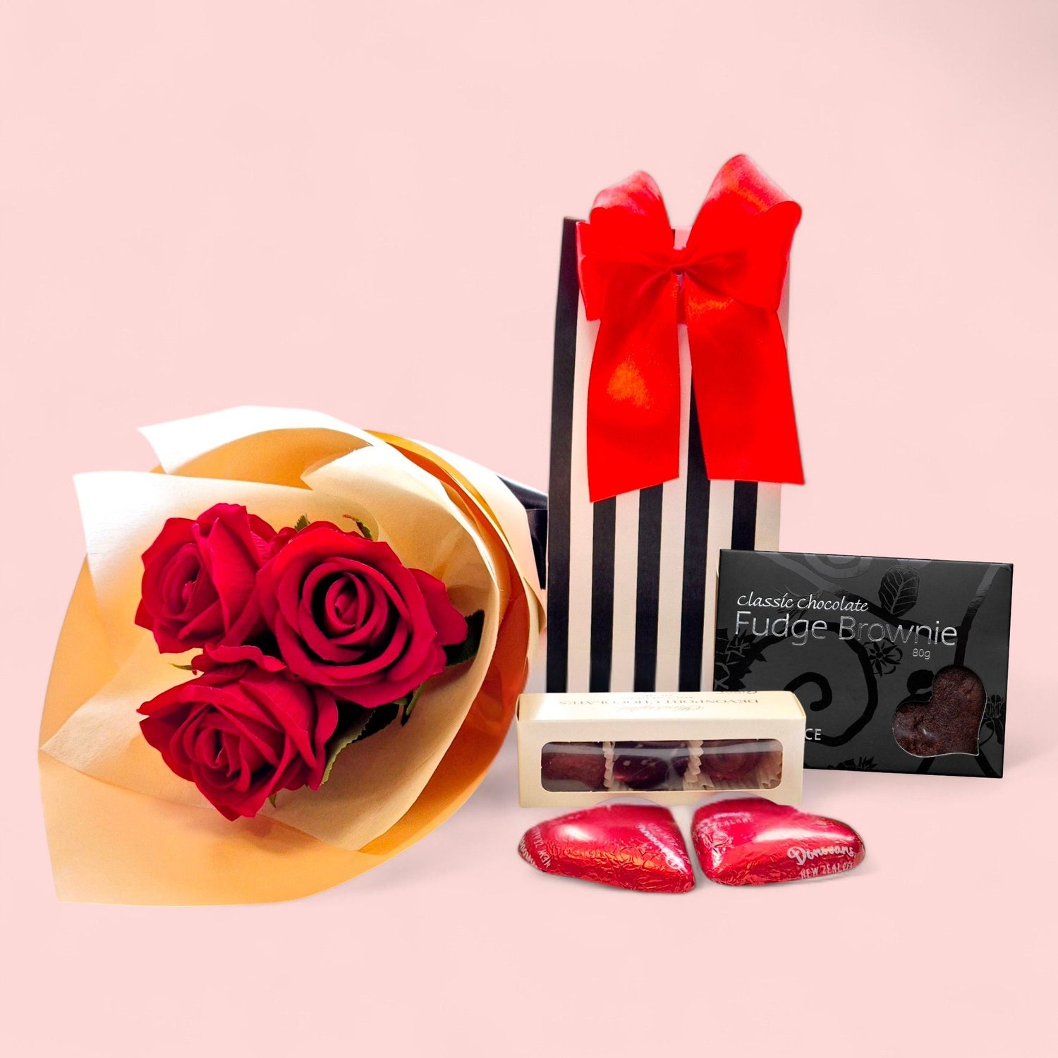 Black-and-white gift bag filled with a chocolate treat and a brownie, accompanied by three beautifully wrapped artificial red roses, perfect for Valentine’s Day gifting.