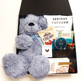 Baby love gift basket with blue teddy, honey, popcorn, biscuits & nibbles. Presented in a modern gift box.
